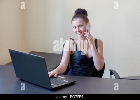 Nette junge büroangestellte im Abendkleid Gespräch am Handy im Büro Stockfoto