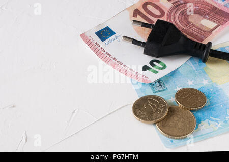 Sparen bei der Stromrechnung Konzept: Steckdose über Euro-Scheine und -Münzen Stockfoto