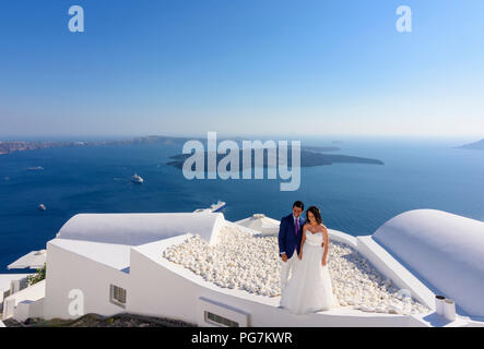 Ein Hochzeitspaar Pose auf der Dachterrasse von einem weiß getünchten Gebäude mit Blick auf die Caldera von Santorin Stockfoto