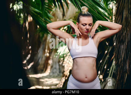 Junge attraktive blonde Frau in Weiß sportswear Yoga Pilates Fitness Übungen in der tropischen Natur. Pre natal trainieren, gesunden Lebensstil, rec Stockfoto