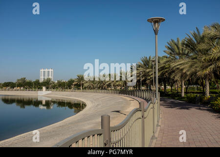 Gepflasterter Weg neben einem künstlichen Teich in Al Barsha Pond Park, Dubai, Vereinigte Arabische Emirate Stockfoto