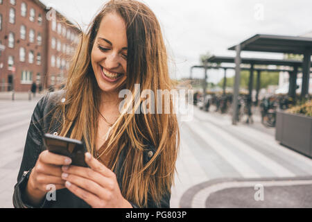 Glückliche junge Frau mit Handy in der Stadt Stockfoto