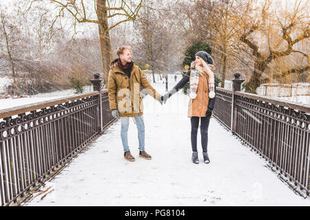 Junges Paar in der Liebe stehen Hand in Hand über die Fußgängerbrücke in einem Park an einem verschneiten Tag Stockfoto