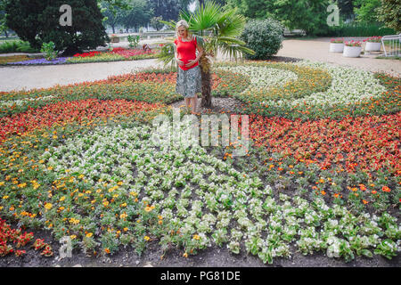 Schwangere Frau steht man inmitten blühender Blumen im Park Stockfoto