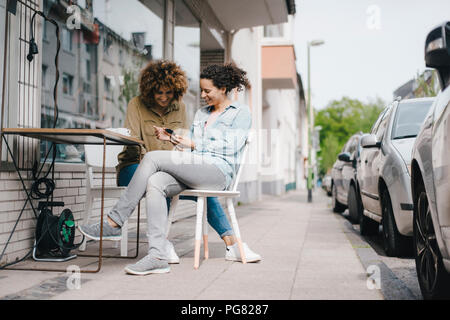 Zwei Freunde, die in Coworking Space, am Tisch sitzend mit Kaffee, mit Smartphone Stockfoto