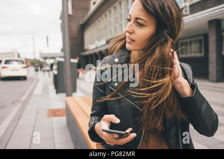 Junge Frau mit windswept Haar holding Handy in der Stadt Stockfoto
