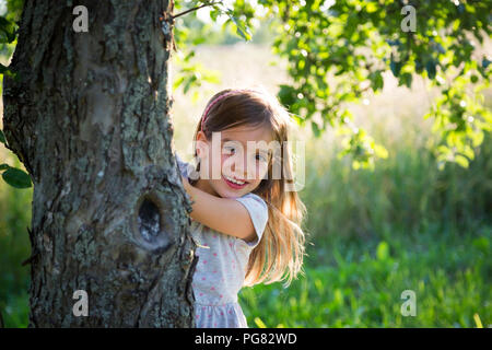 Junge Mädchen hinter dem Baumstamm bei sommerlichen Abend Stockfoto