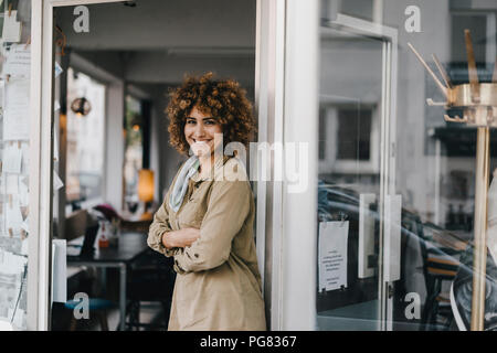 Lächelnde Frau mit der Waffe in der Tür des Coworking Space gekreuzt Stockfoto