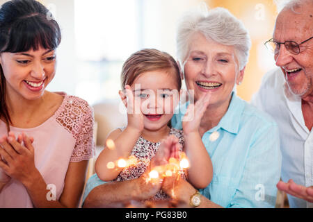 Kleines Mädchen lwatching Wunderkerzen auf einen Geburtstagskuchen, sitzen auf der Großmutter die Runde Stockfoto