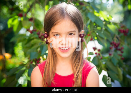 Kleines Mädchen mit Kirschen auf den Ohren Stockfoto