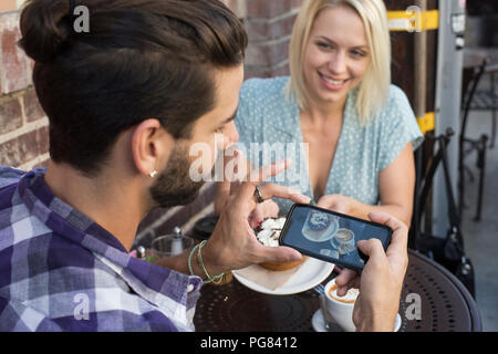 Junger Mann mit Freundin unter Handy Bild bei Café im Freien Stockfoto
