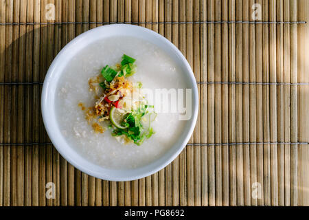 Thai Reis congee oder Reisbrei mit Zutaten würzen. (Fischsauce, gebratenem Knoblauch, Chili, Paprika, Frühlingszwiebeln, Koriander und Limette). Stockfoto