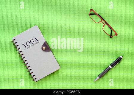 Yoga workout Buch Konzept anmelden, Flach, oben Yoga workout Buch, Brille, Stift auf Yoga Matte Hintergrund anmelden. Stockfoto