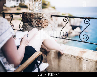 Frau auf der Terrasse über das Meer schreiben oder Notizen mit Stift Stockfoto