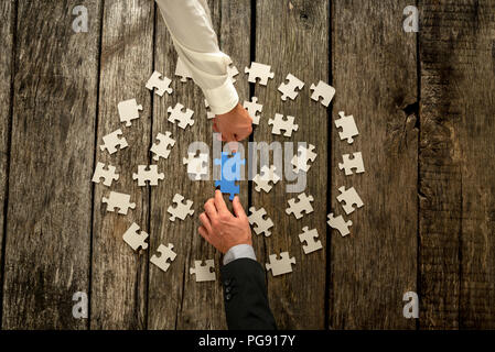 Teamarbeit in Business Konzept mit zwei Geschäftsleute um einen Kreis der zerstreuten weißen Puzzleteile Kooperierenden einen blauen Jigsaw im Centr zu konstruieren Stockfoto