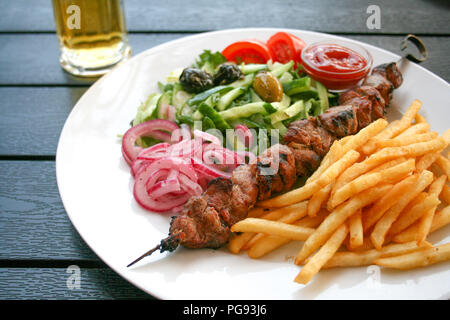 Schaschlik oder shashlyk von Schweinefleisch, Schüssel, aufgespießt und gegrillt Cubes von Fleisch, mit roten Zwiebeln, Gemüse, Tomaten, Oliven und Pommes frites auf einer hölzernen ta Stockfoto