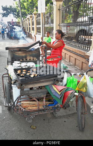 Cebu, Philippines-October 18, 2016: streetfood Verkäuferin kocht und verkauft Philippinischen Köstlichkeiten aus ihrer Nahrung Fahrrad - Warenkorb angeheizt durch Brennholz stationiert Stockfoto