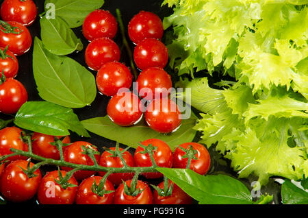 Cherry Tomaten und Kopfsalat in Wasser zum Waschen, Ansicht von oben auf einem dunklen Hintergrund Stockfoto