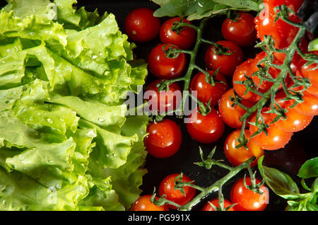 Cherry Tomaten und Kopfsalat in Wasser zum Waschen, Ansicht von oben auf einem dunklen Hintergrund Stockfoto