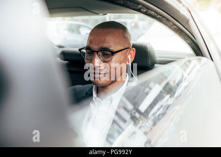 Business Person tragen Brillen in seine Limousine sitzen auf Rücksitz zu Office. Mann mit Ohrhörer Managing Business Arbeit in Bewegung sitzen Stockfoto