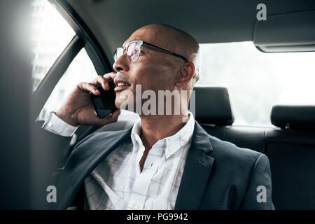 Unternehmer tragen Brillen Sprechen über Handy in seiner Limousine sitzend Blick aus dem Fenster. Mann Managing Business auf Handy sitzt in c Stockfoto