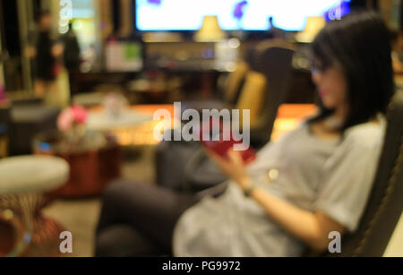 Unscharf geschossen von einer jungen Frau in der Lobby mit Blick auf Handy in der Hand, für Hintergrund Stockfoto