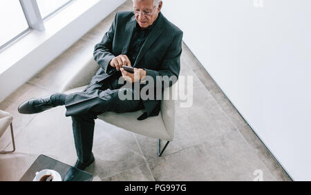 Hohe Betrachtungswinkel der älteren Geschäftsmann SMS mit dem Mobiltelefon. Ausgereifte Corporate professionelle Lesen von E-Mails auf seinem Smartphone während der Pause. Senior m Stockfoto