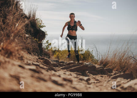 Passende Frau läuft auf den Berg Trail. Weibliche Athleten üben querfeldein laufen auf einem felsigen Trail. Stockfoto