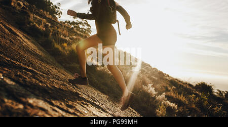 Frau auf einem felsigen Berghang. 7/8 shot der weiblichen Trail Runner läuft bergauf an einem sonnigen Tag. Stockfoto