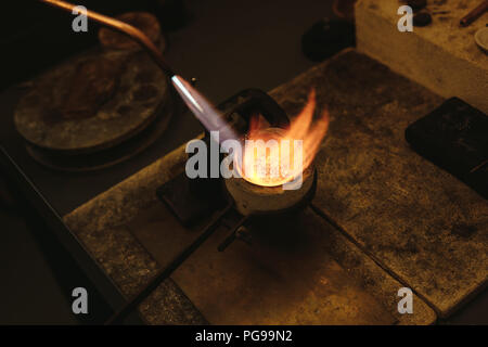 Schmelzen von Gold in einem kleinen Tiegel für die Herstellung von Schmuck. Goldschmied mit Flamme zu Erhitzen der silbernen Körner in einem Tiegel schmelzen und. Stockfoto