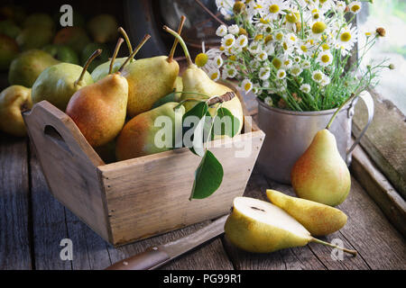 Frische Birnen in einer Holzkiste und Strauß Gänseblümchen auf hölzernen Tisch in der Nähe der Fenster im Inneren der retro Haus im Dorf. Stockfoto