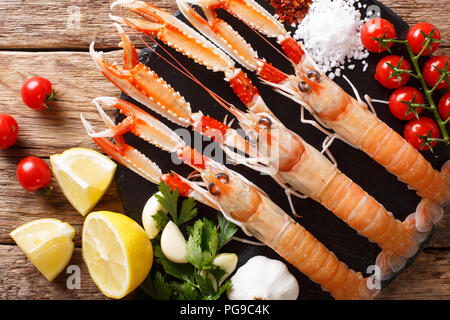 Wunderschönen frische rohe Scampi, Scampi mit Gemüse der Saison und Kräuter closeup auf ein Brett auf einem Holztisch. horizontal oben Ansicht von oben Stockfoto