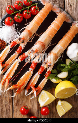 Wunderschönen frische rohe Scampi, Scampi mit Gemüse der Saison und Kräuter closeup auf ein Brett auf einen hölzernen Tisch. Vertikal oben Ansicht von oben Stockfoto