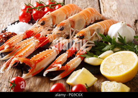 Wunderschönen frische rohe Scampi, Scampi mit Gemüse der Saison und Kräuter closeup auf ein Brett auf einem Holztisch. Horizontale Stockfoto