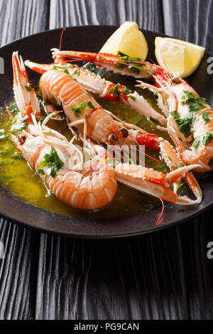 Gourmet Meeresfrüchte Scampi oder Scampi oder Kaisergranat sind auf einer schwarzen Platte, mit Soße und Zitrone in der Nähe serviert. Vertikale Stockfoto