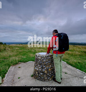 Ein Männer mittleren Alters Wanderer mit Rucksack, bewundern Sie die Aussicht von Beacon Hill und Harting nach unten entlang des South Downs Way. Hampshire, Großbritannien Stockfoto