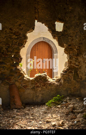 Eine alte hölzerne gewölbten Tür in Sizilien durch ein defektes Öffnung in einer Steinmauer gesehen Stockfoto