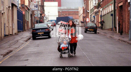 Eine Frau mit einem Baby im Kinderwagen eilt ein Speichern unsere Jobs Rally für den Rover Werk in Longbridge, Birmingham, April 2000 Stockfoto