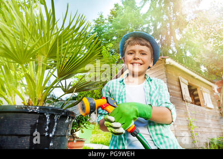 Happy Boy Bewässerung Palm Tree mit Hilfe der Sprinkleranlage Stockfoto