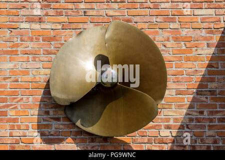 Ein Messing Propeller aus einem Start auf einer Ziegelwand Hintergrund. Website über das Meer, Schiffe, Angeln, Natur, Industrial Design. Stockfoto