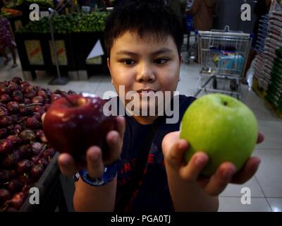 Foto einer jungen asiatischen Jungen hält eine rote und grüne Apple in einem Supermarkt. Stockfoto