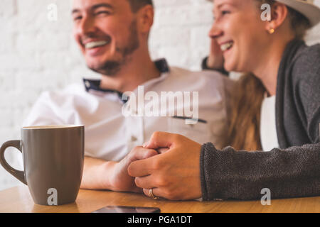 Der Mann hält eine weibliche Hand in der Hand. Vor dem Hintergrund des lächelnden, fröhliche Mann und das Mädchen sind sichtbar. Vor ihnen auf dem Tisch Telefon liegt Stockfoto