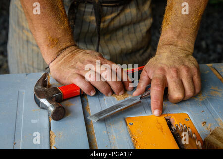 Die Hände des Menschen fallen in den Staub mit einem Hammer und einem Meißel auf dem Tisch gesehen. Zimmerei tools, Konzept aus Holz arbeiten. Stockfoto