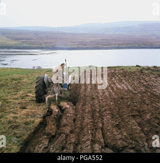 1960, historische, Bauer auf dem Traktor pflügen ein Feld durch ein Loch auf der Insel Skye, Highlands, Schottland, UK. Stockfoto