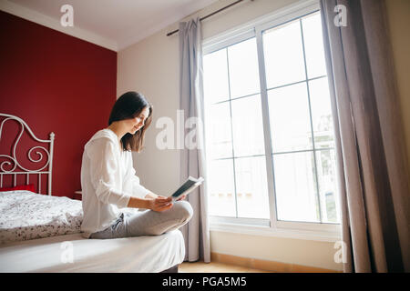 Frau liest Buch auf dem Bett am Morgen. Ferienhäuser Konzept Stockfoto