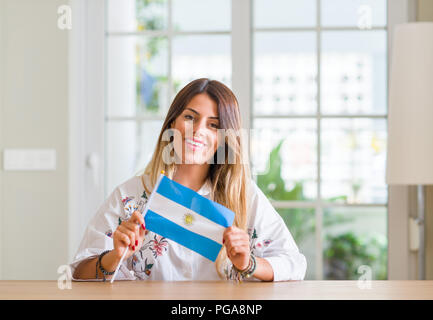 Junge Frau zu Hause holding Flagge Argentinien mit einem glücklichen Gesicht stehen und lächelnd mit einem selbstbewussten lächeln zähne Stockfoto