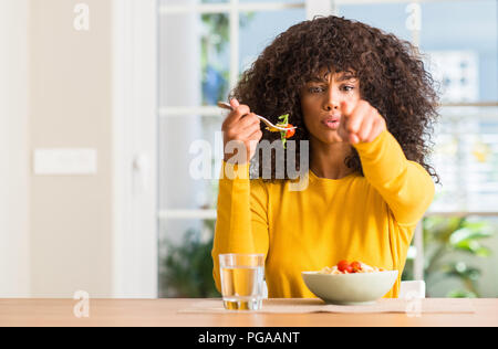 Afrikanische amerikanische Frau essen Pasta Salat zu Hause mit dem Finger an die Kamera und an Sie gerichtet, Handzeichen, positiv und zuversichtlich Geste aus dem Fr Stockfoto