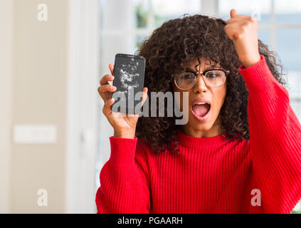 African American woman holding gebrochen Smartphone genervt und frustriert schrie mit Zorn, verrückt und schreien mit erhobener Hand, Wut Konzept Stockfoto