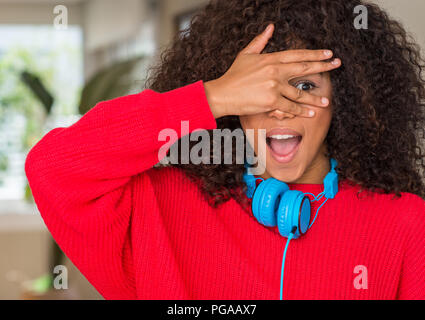 Afrikanische amerikanische Frau mit Kopfhörern peeking im Schock für Gesicht und Augen mit der Hand, schauen durch die Finger mit peinlich Ausdruck. Stockfoto