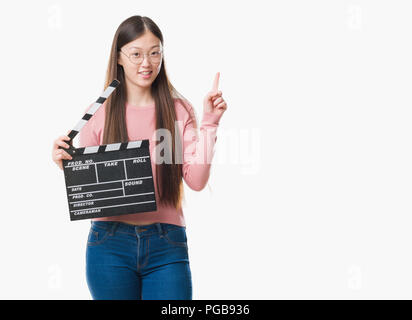 Junge chinesische Frau über isolierte Hintergrund Holding 1880 Mit einer Idee oder Frage Zeigefinger mit glücklichen Gesicht überrascht, Nummer eins Stockfoto